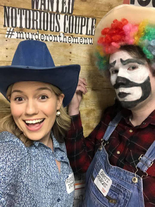 A cowboy and a clown stand in front of a backdrop.